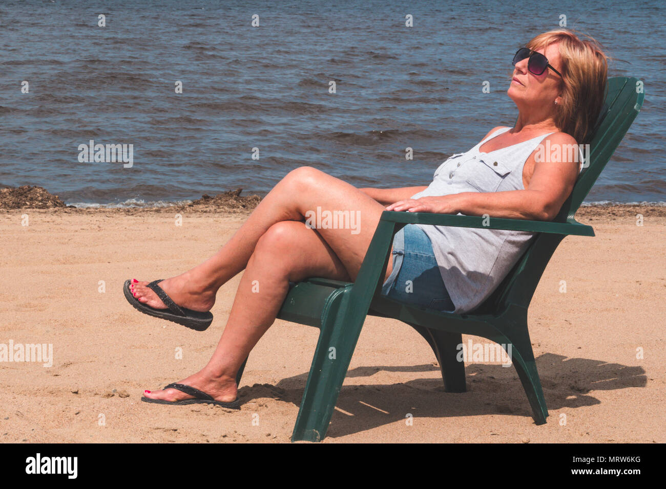 Donna in pensione in vacanza seduto alla spiaggia Lago Maskinonge St-Gabriel-de-Brandon Québec Canada Foto Stock