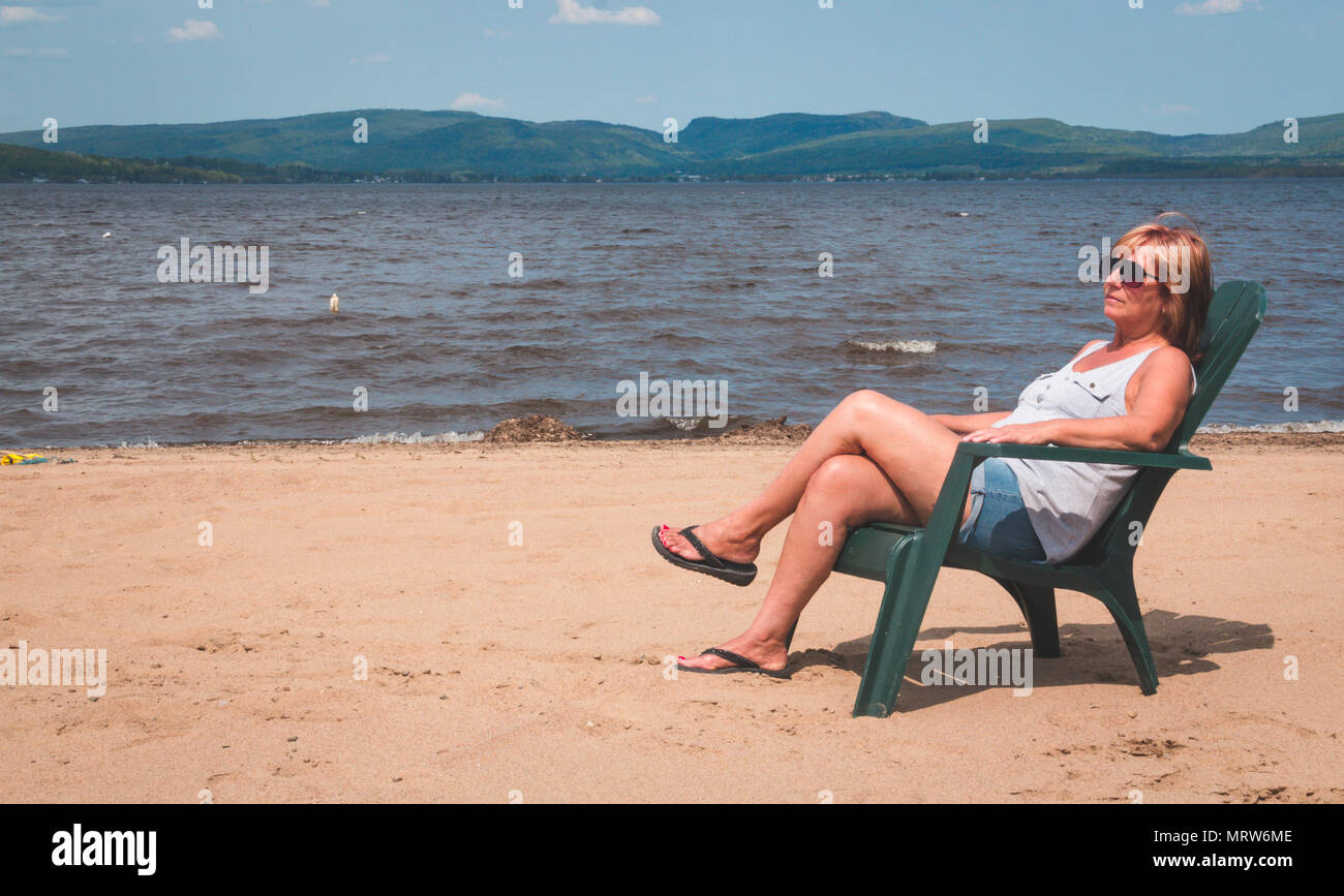 Donna in pensione in vacanza seduto alla spiaggia Lago Maskinonge St-Gabriel-de-Brandon Québec Canada Foto Stock