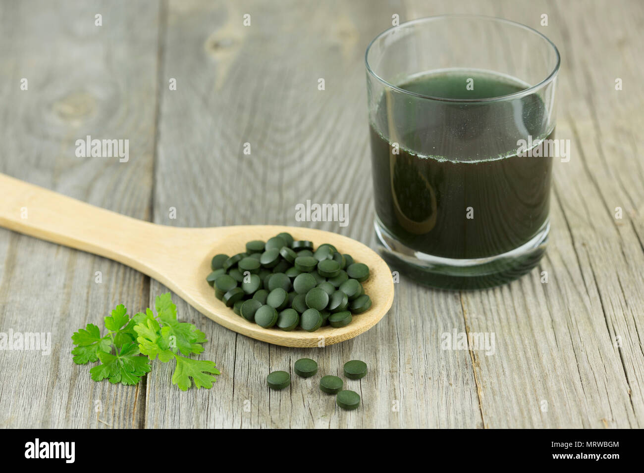 La clorella, acqua fresca alghe, pellet sul cucchiaio di legno liscio con prezzemolo e sciolto in acqua il vetro Foto Stock