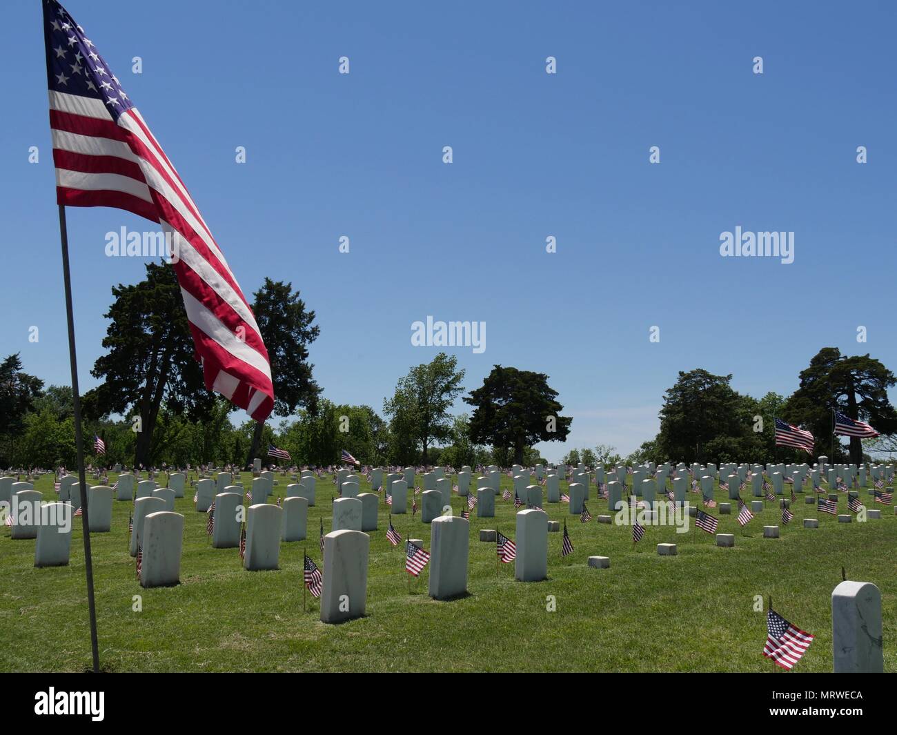 Un grande United States Flag e piccole bandiere statunitensi accanto alle lapidi a Fort Gibson Cimitero Nazionale in Muskogee, Oklahoma Foto Stock