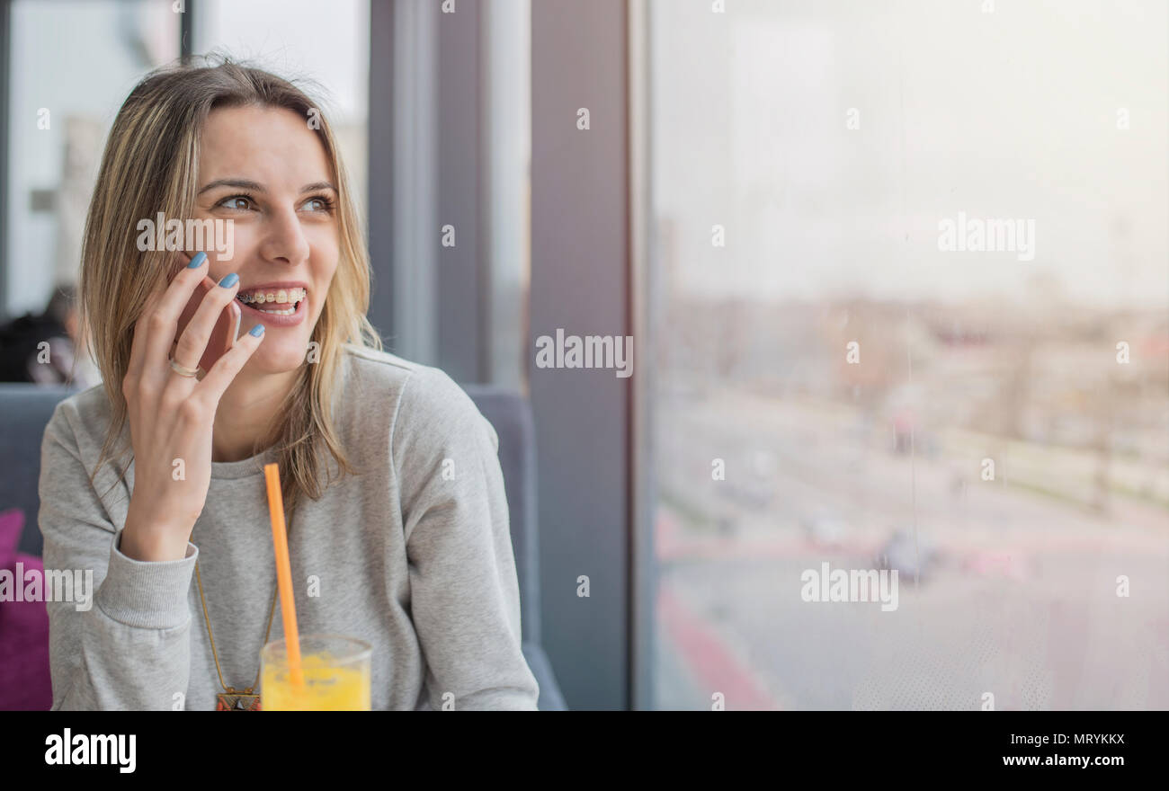 Bella ragazza sorridente seduto e parlando al telefono cellulare in un coffee shop, ristorante. Tempo di ragazze, godendo in giornata soleggiata. Foto Stock