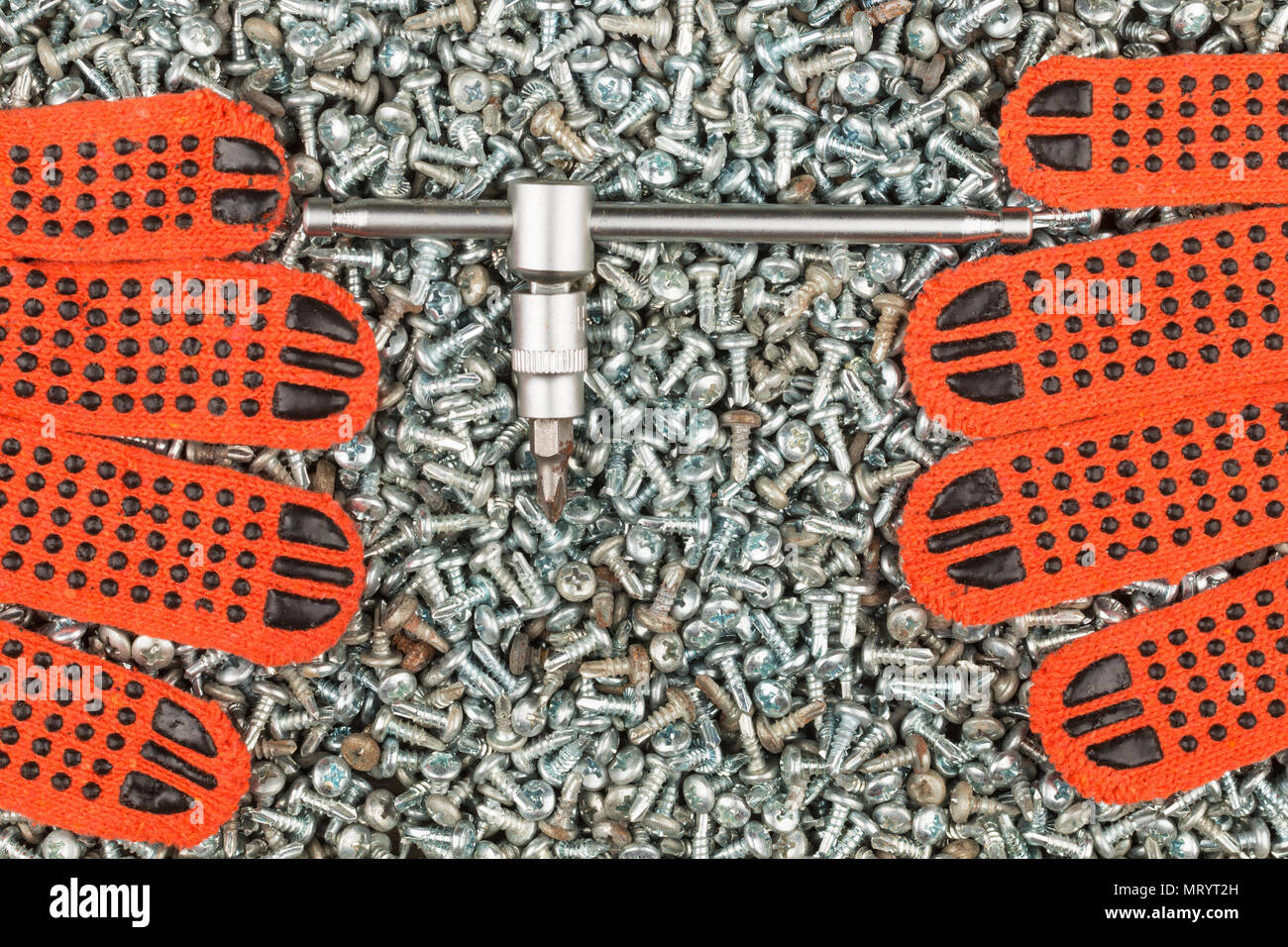 Guanti da lavoro e un cacciavite giacente su un mucchio di viti. Vista da sopra Foto Stock
