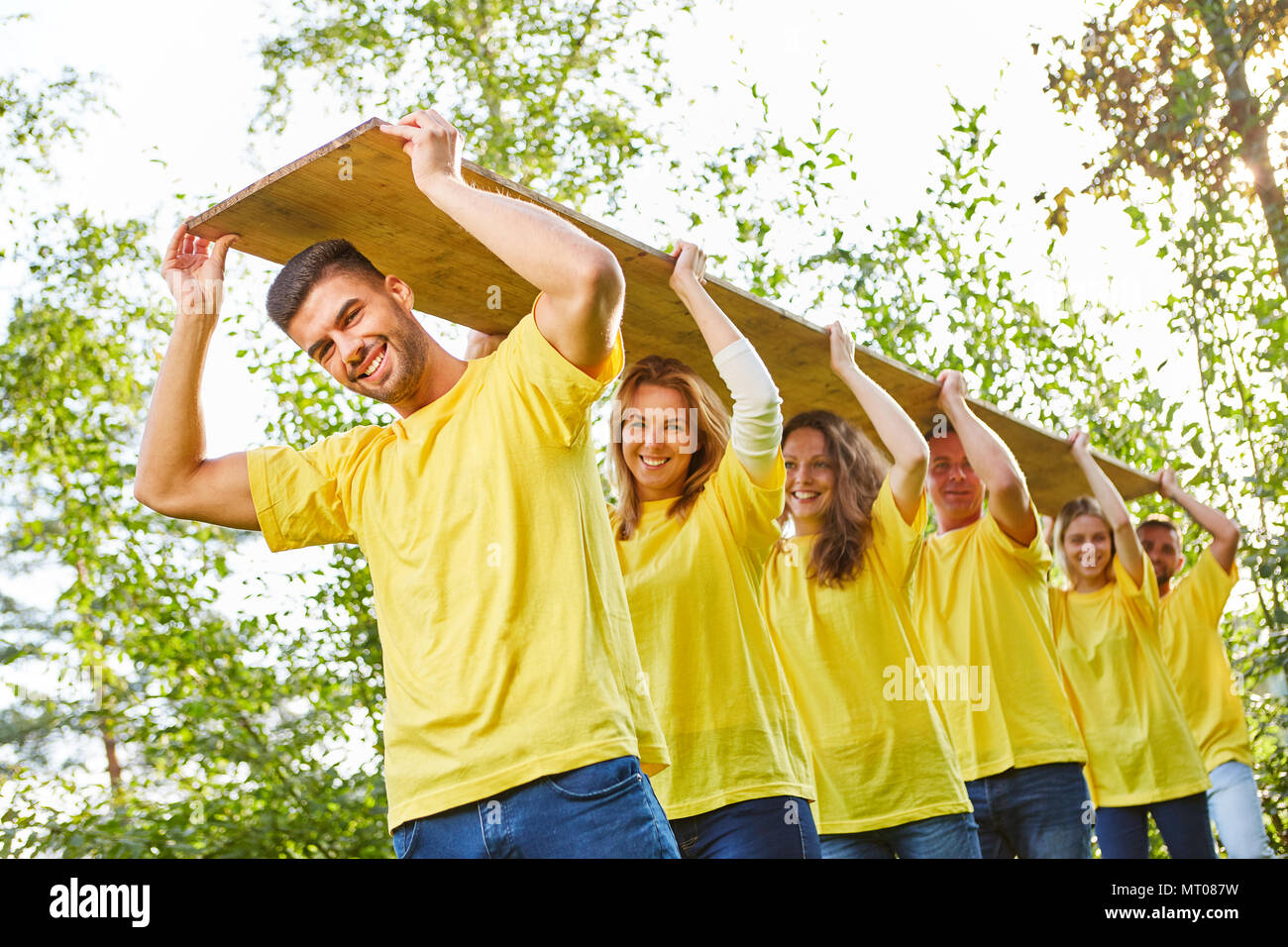 Il giovane equipaggio porta una tavola di legno in un gioco al teambuilding workshop Foto Stock