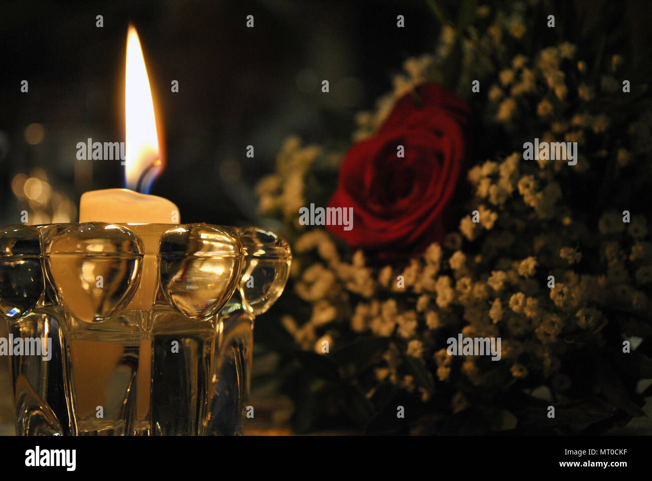 Decorazione di un cero bianco illuminazione di un bouquet di fiori con una rosa bianca in background Foto Stock