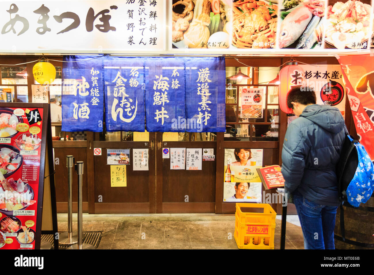 Piscina Omicho Ichiba, Omicho freschi di mercato alimentare a Kanazawa, Giappone. Uomo che guarda al di fuori del menu tipico ristorante Giapponese serve bocce di alimenti per pesci. Foto Stock