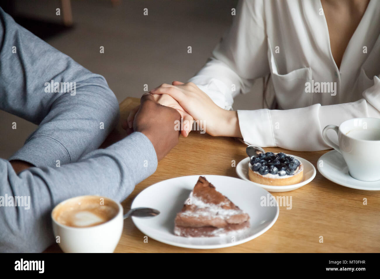 Interracial giovane holding hands seduti al tavolo del bar, primo piano Foto Stock