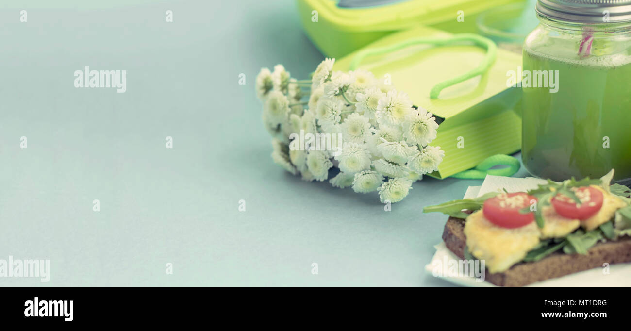Banner sana colazione vegetariana panino pane di grano di formaggio di tofu, detox smoothie, semi di zucca, pomodori ciliegini, fiori naturali, sfondo blu Foto Stock