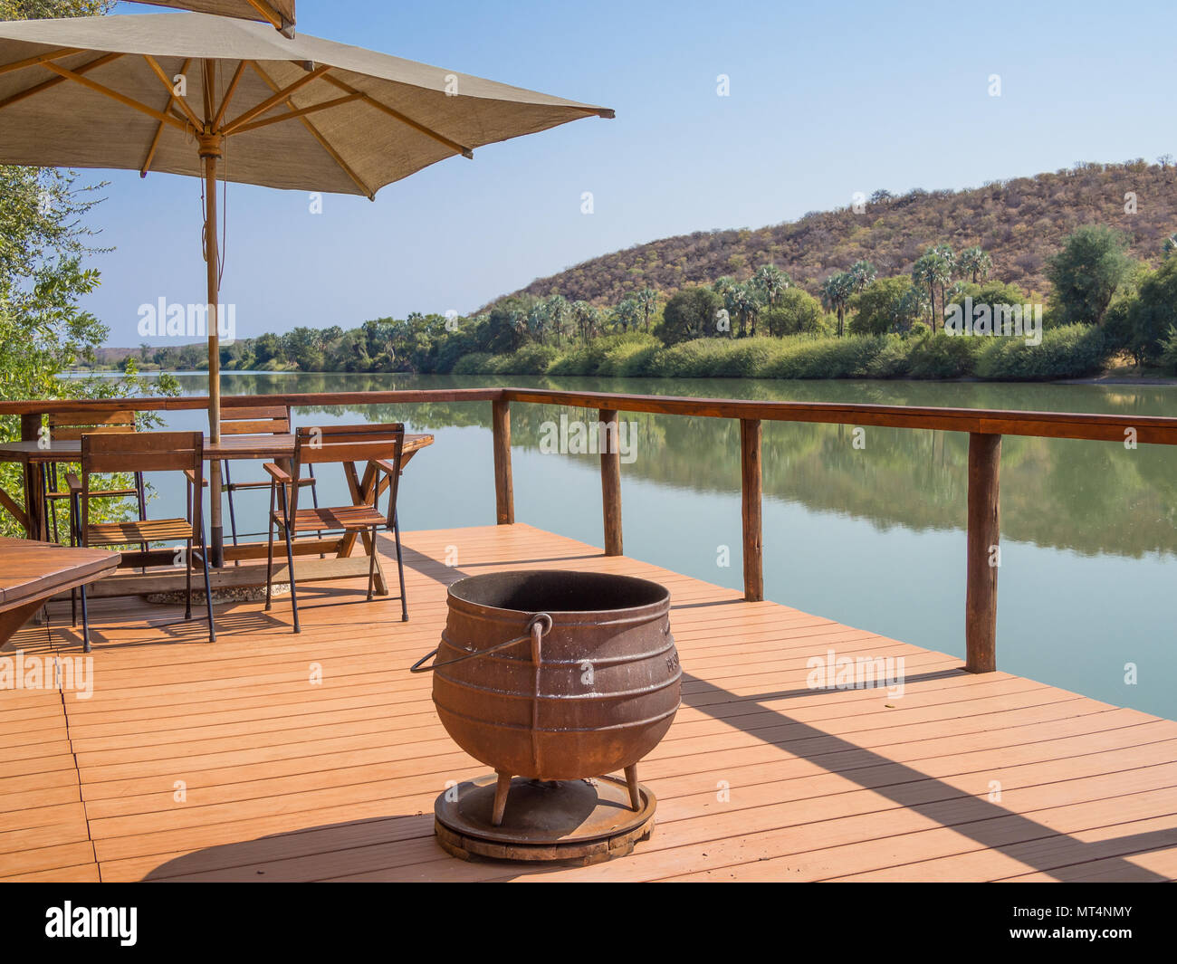 Ruacana, Namibia - Luglio 22, 2015: terrazza in legno con sedie, umbrealla, tavolo e ghisa pot presso il fiume Kunene Foto Stock