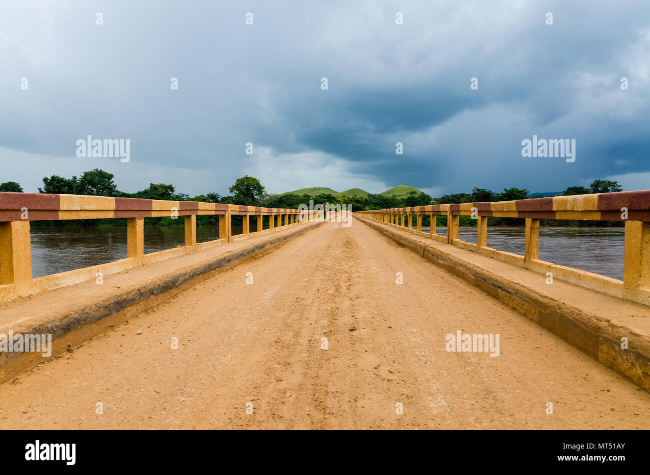 Semplice strada sterrata ponte sul fiume tropicale con enormi nubi nella Repubblica del Congo, Africa Foto Stock