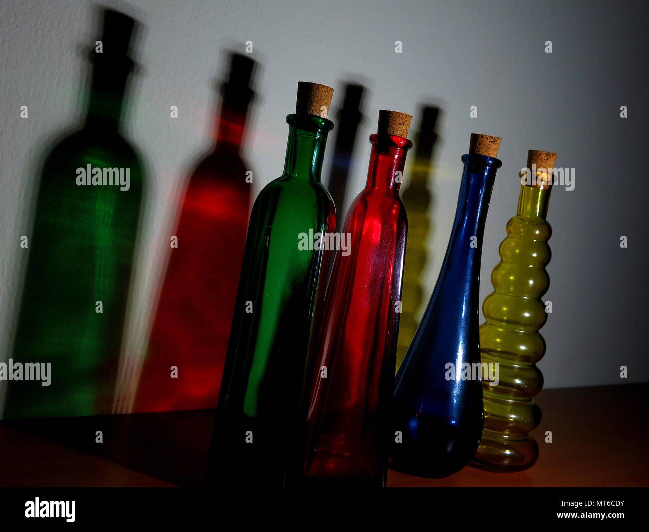 Bottiglie colorate che gettano ombre sulla parete. Foto Stock
