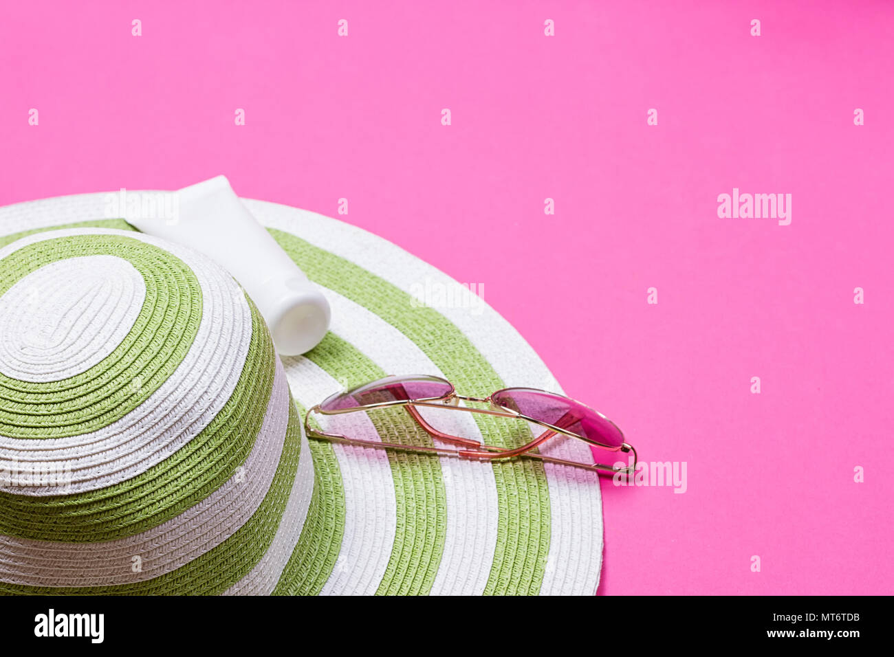 Cappello di paglia e blocco sun lotion tubo e occhiali da sole su un sfondo rosa Foto Stock