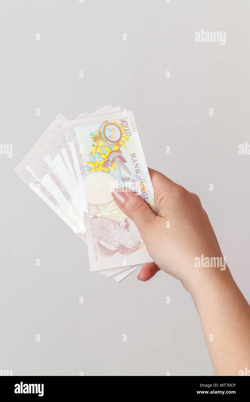 Dieci pound note della Bank of England in mano femminile. Close-up foto su uno sfondo grigio con il fuoco selettivo Foto Stock