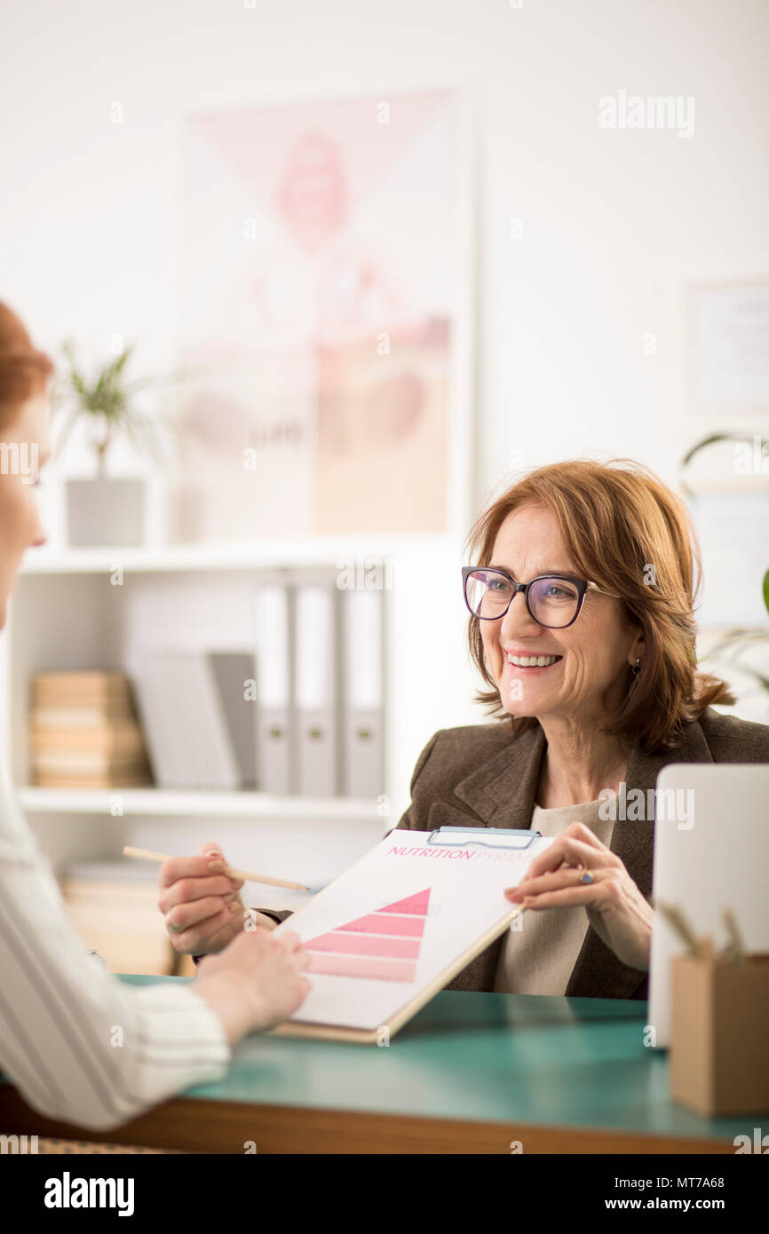 Professional donna che mostra una piramide nutrizionale per il suo paziente durante l'appuntamento Foto Stock