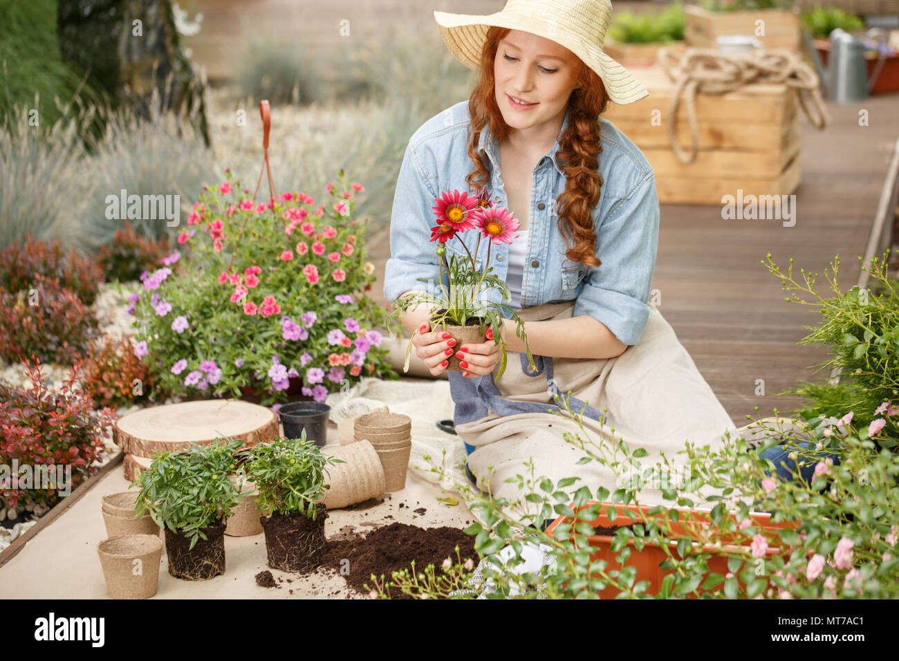 Giovane donna tenendo un vaso di fiori, semina e guardando dopo la sua casa giardino con terrazza Foto Stock