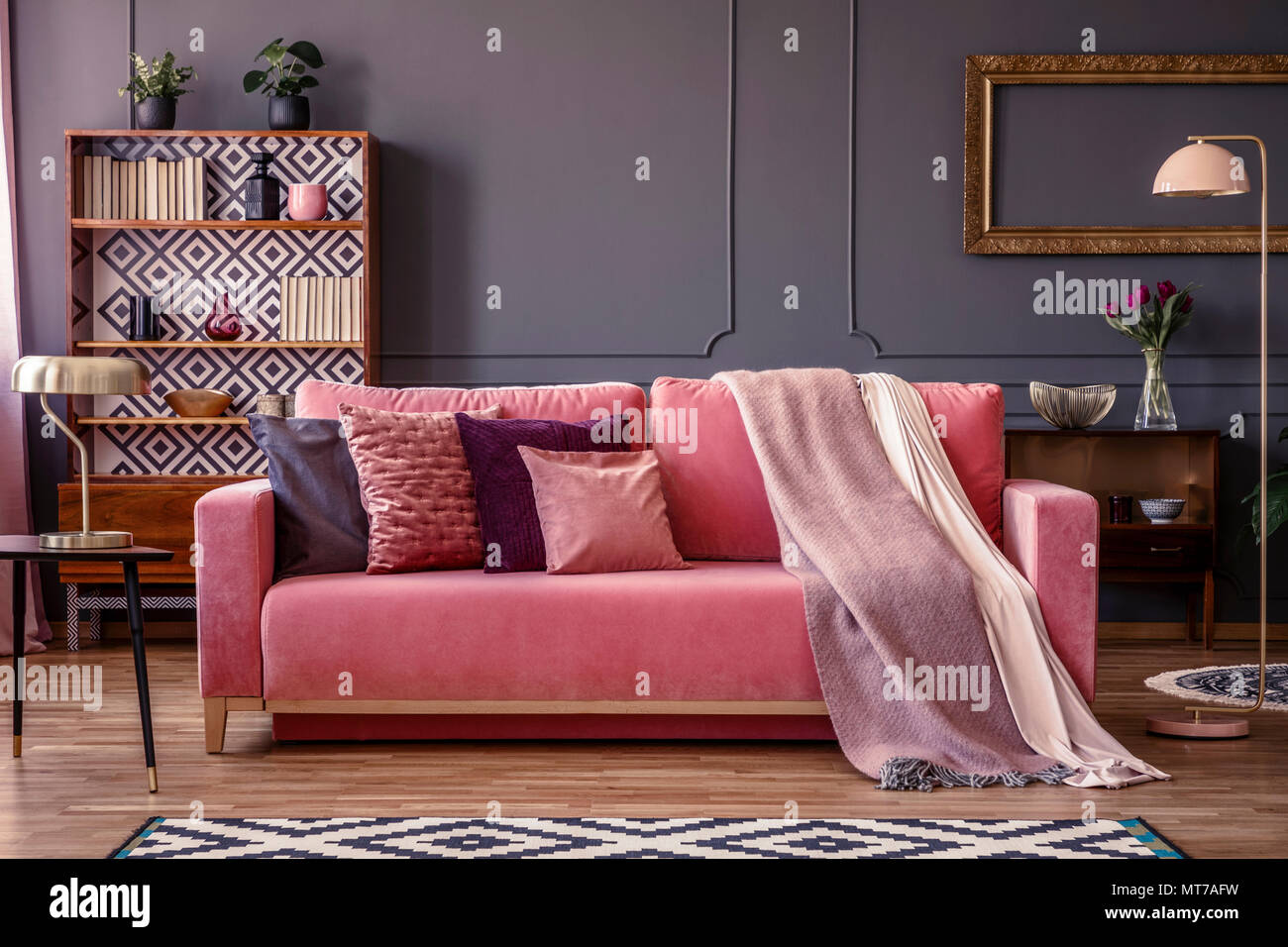 Vista frontale di un rosa divano con cuscini e coperte, vintage credenza in background in un elegante salotto interno Foto Stock