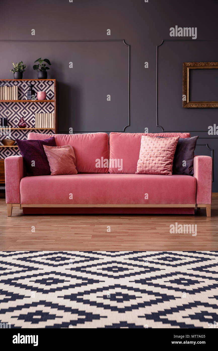 Tappeto a motivi geometrici di fronte un divano rosa con cuscini in un elegante salotto interno con stampaggio a parete e credenza in background Foto Stock