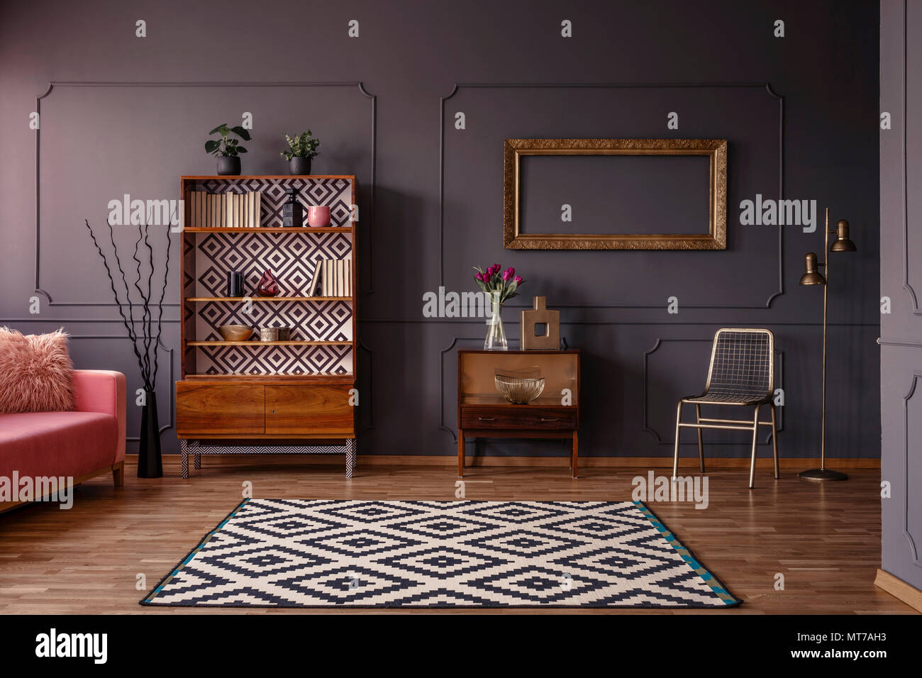 Vintage salotto interno con un tappeto a motivi geometrici, credenza, cornice dorata sulla parete, sedia e stampaggio a parete Foto Stock