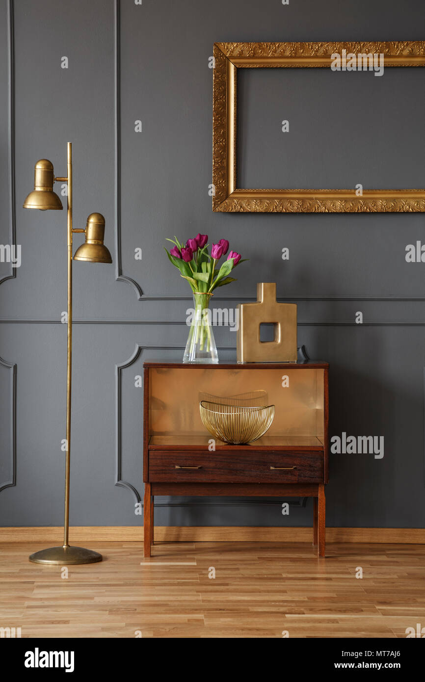 Armadio in legno decorato con fiori e vaso accanto a una lampada in un corridoio interno con stampaggio a parete una cornice dorata Foto Stock