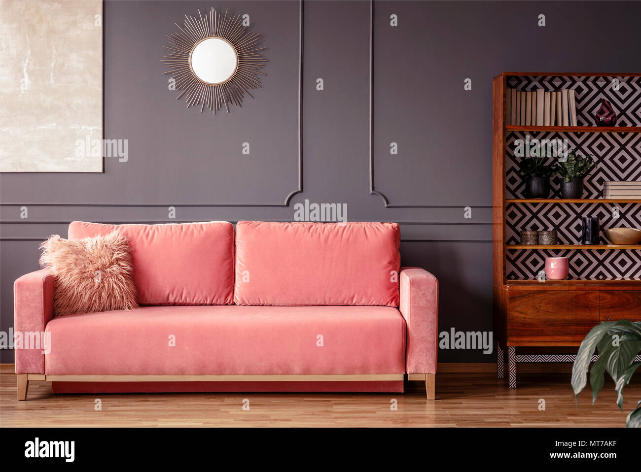 Semplice, rosa divano con una pelliccia cuscino accanto a un armadio in legno in salotto interno con muro grigio e specchio Foto Stock
