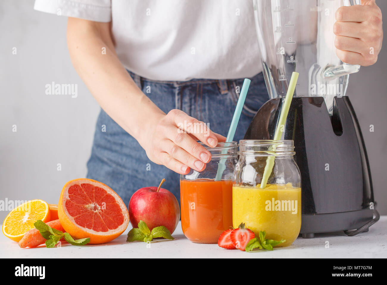 La donna è la cucina estiva multicolore di succhi di frutta o frullati in vasetti di vetro e gli ingredienti sul tavolo bianco. Foto Stock