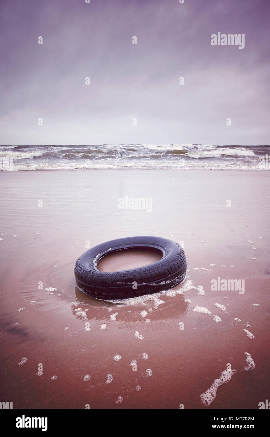Vecchio pneumatico in gomma nero a sinistra su una spiaggia, ambiente inquinamento concetto, il fuoco selettivo nei toni del colore dell'immagine. Foto Stock