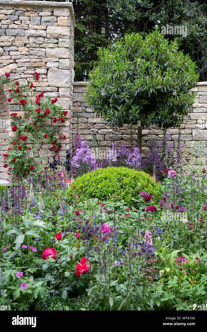 Un secco di nicchia in pietra circondato da multi-piante colorate nelle rivendicazioni ragazzi-molto giardino inglese della RHS Chelsea Flower Show 2018, London, Regno Unito Foto Stock