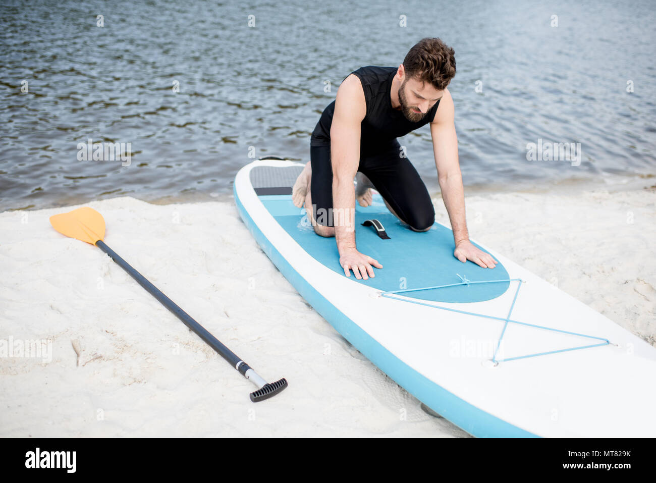 Uomo con standup paddleboard sulla spiaggia Foto Stock