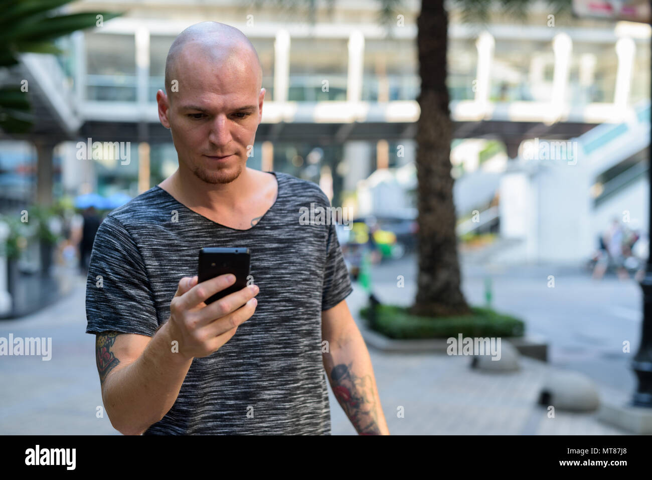 Bel giovane uomo calvo tramite telefono cellulare al di fuori del centro commerciale di t Foto Stock