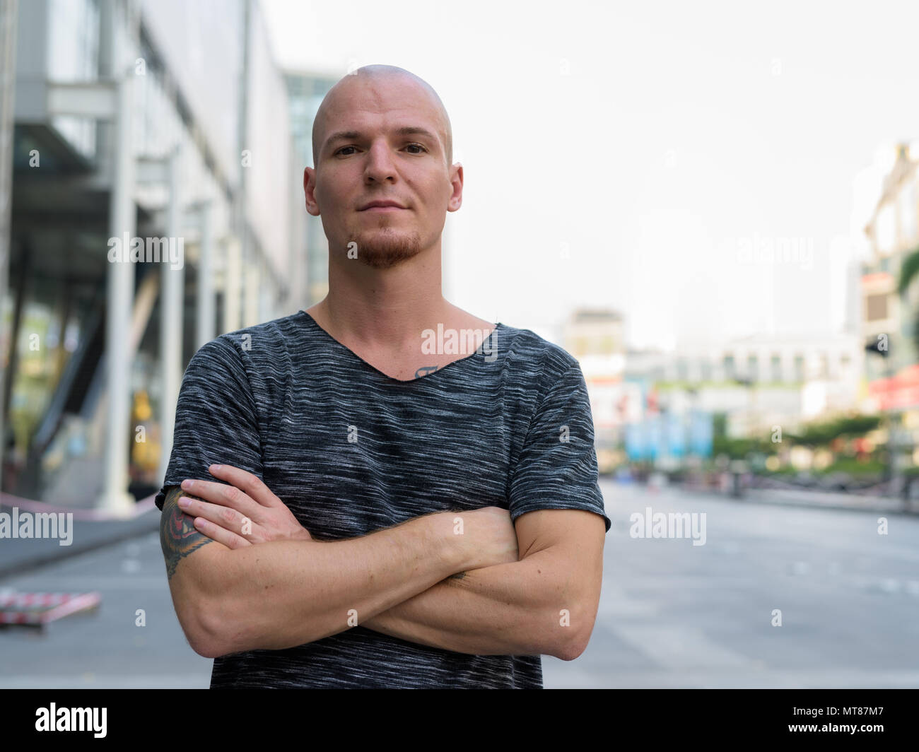 Bel giovane uomo calvo con le braccia incrociate al di fuori del centro commerciale in Foto Stock