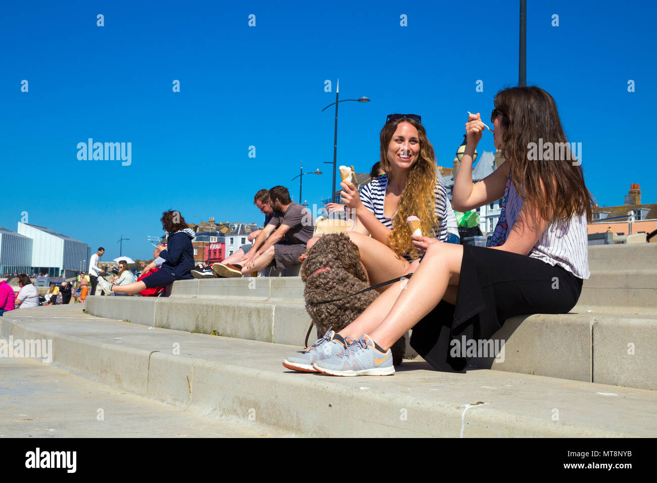 Due donne e un cane seduto di fronte spiaggia a Margate, mangiare il gelato e parlare, Margate, Regno Unito Foto Stock