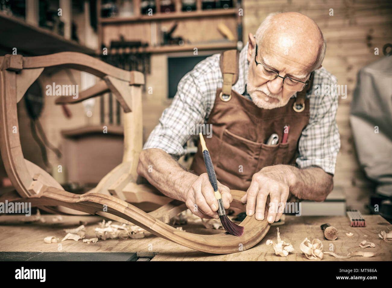 Anziani carpenter utilizza una spazzola su una sedia incompiuto Foto Stock