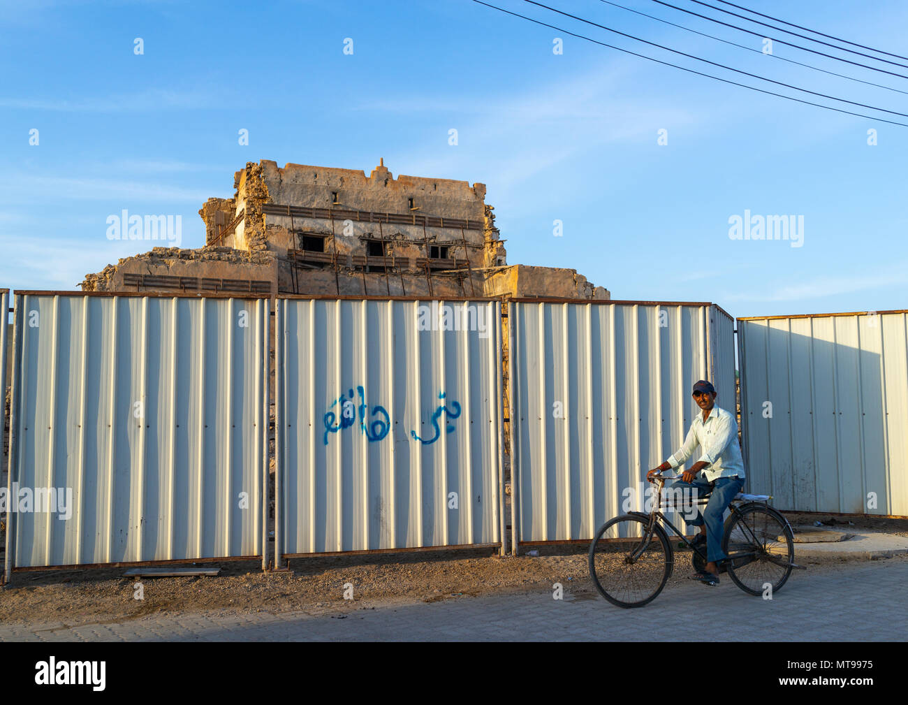 Uomo indiano passando davanti al palazzo vecchio protetti da un recinto, Dhofar Governatorato, Mirbat, Oman Foto Stock