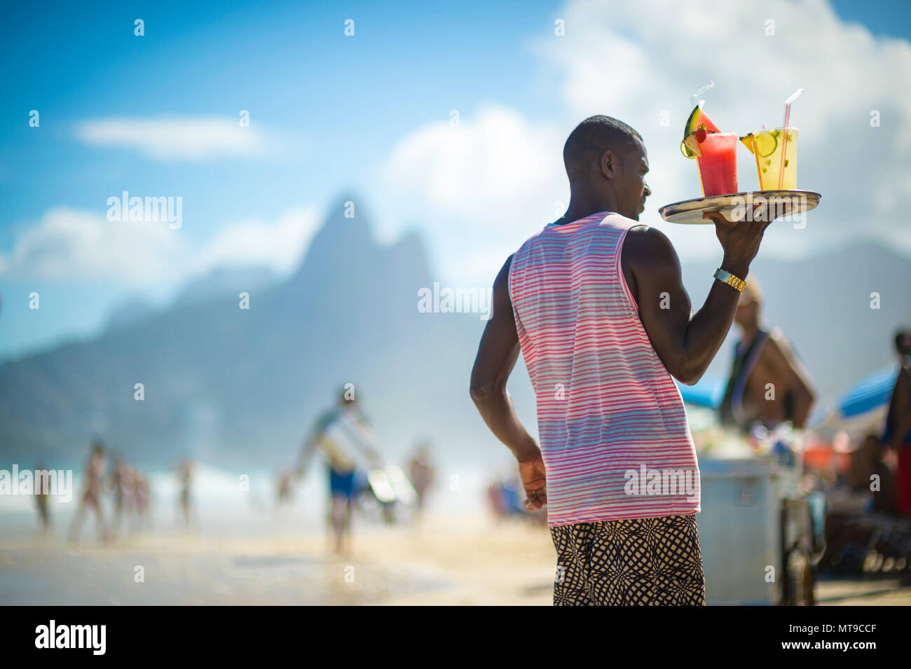 RIO DE JANEIRO - circa marzo, 2018: una spiaggia venditore a vendere caipirinha sulla spiaggia di Ipanema con due fratelli mountain in background. Foto Stock