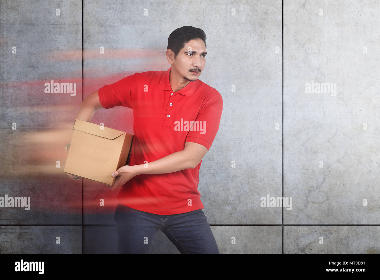 Attraente maschio asiatici courier portare la scatola con sfondo di parete Foto Stock