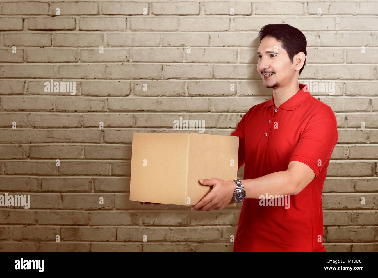 Giovani asiatici corriere maschio tenendo il pacchetto con la parete di fondo Foto Stock