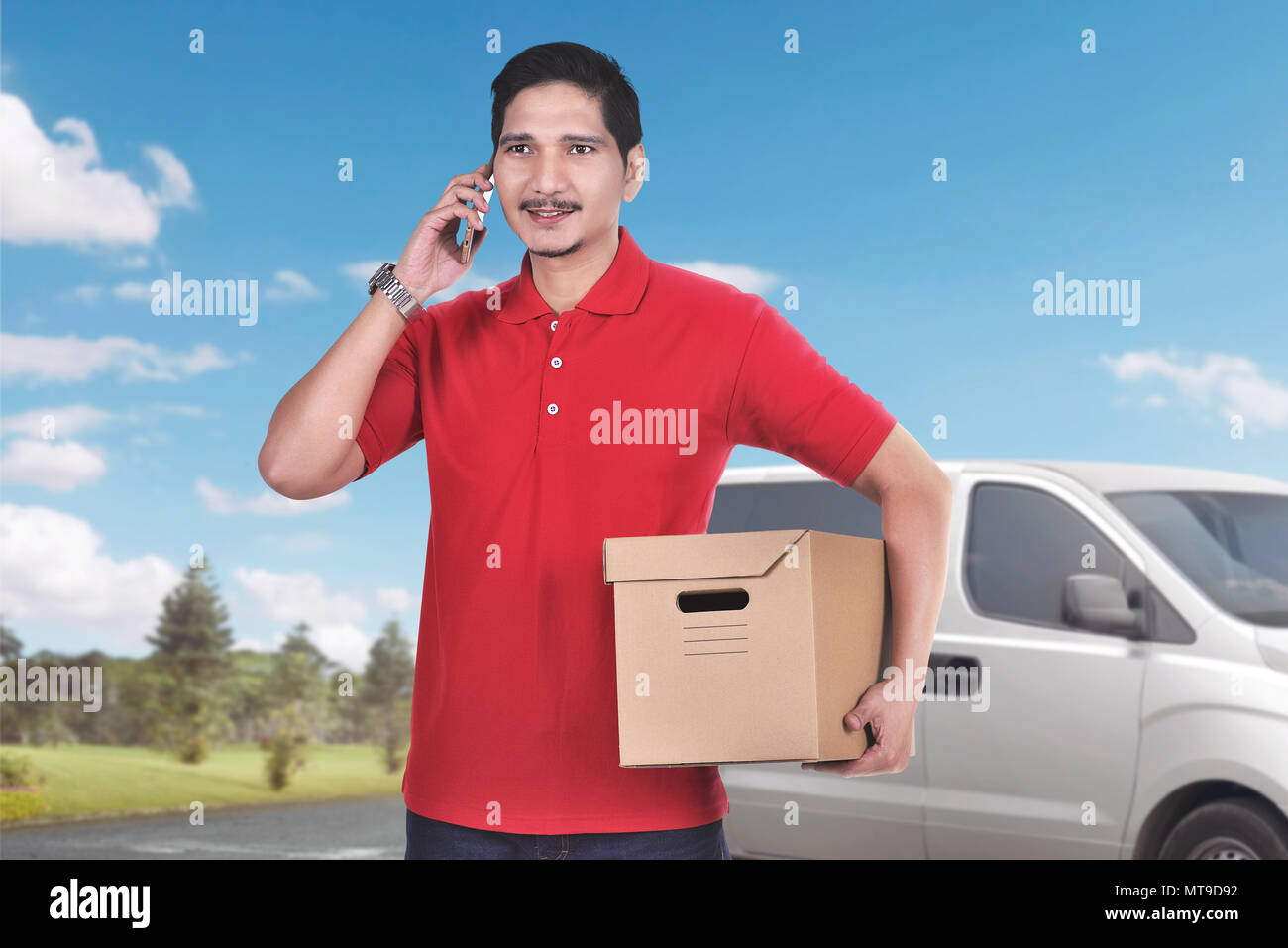 Bella asiatica corriere maschio con telefono portare il pacco con van sullo sfondo Foto Stock