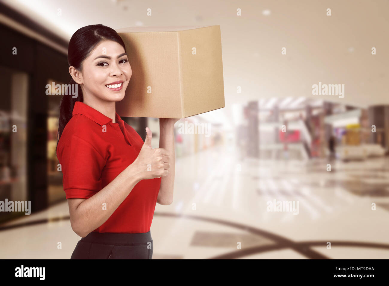 Sorridente corriere asiatico donna che porta il pacco per offrire Foto Stock