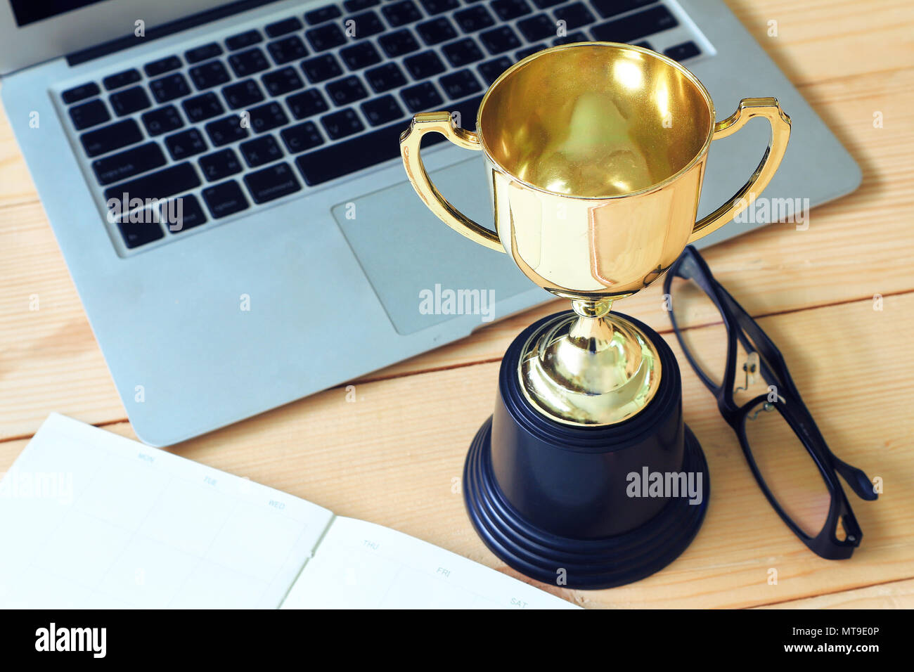 Trofeo e laptop e bicchieri e nota un libro sul tavolo di legno, win concetto. Foto Stock