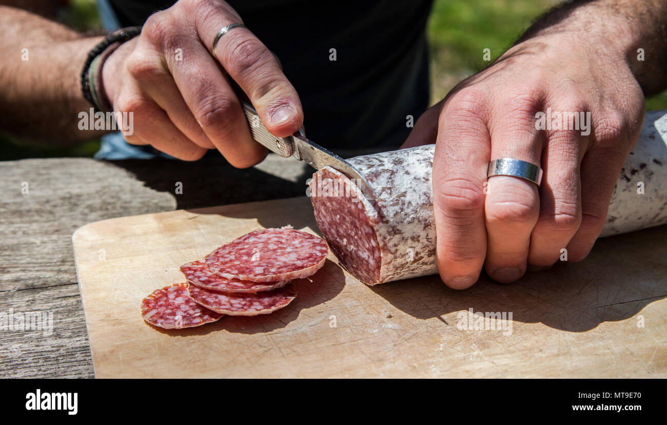 Un uomo taglia alcune fette di salame con un coltello Foto stock - Alamy