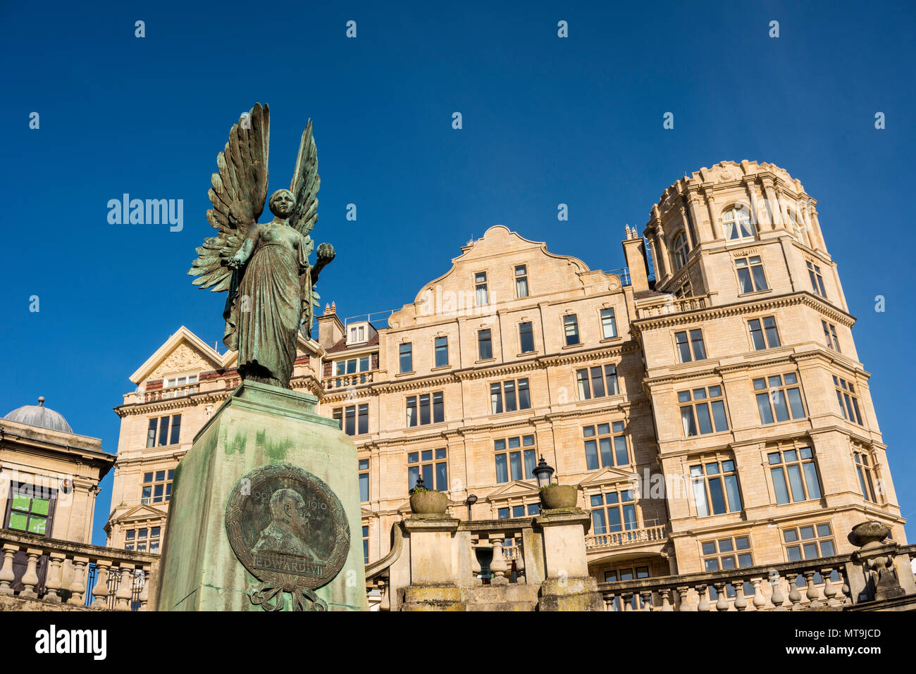 La statua di Angelo della pace in memoria di Edward VII noto come pacificatore in Parade Gardens e Empire Hotel in background, bagno, Somerset, Regno Unito Foto Stock