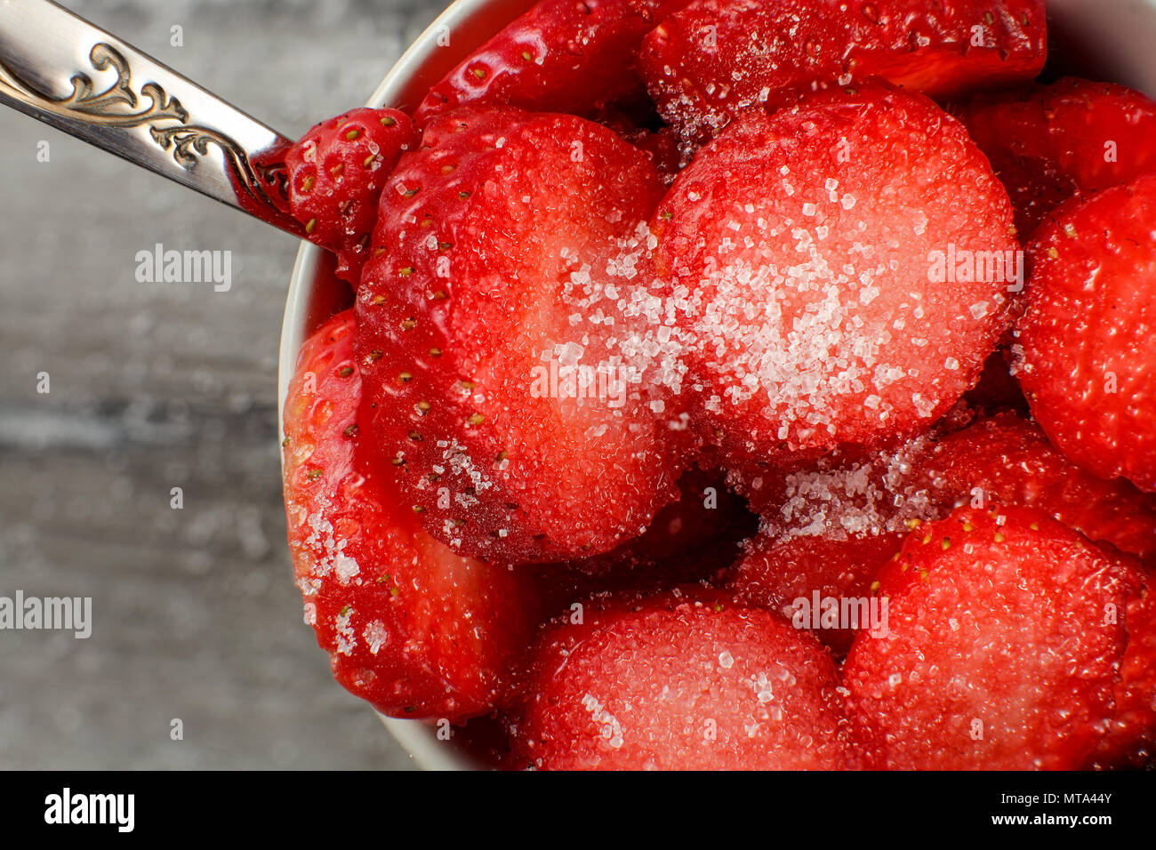 Vista dall'alto in dettaglio su una piccola ciotola con fresche fragole tagliate cosparso con cristallo bianco zucchero, cucchiaio d'argento suggerendo che sono pronti a mangiare. Foto Stock