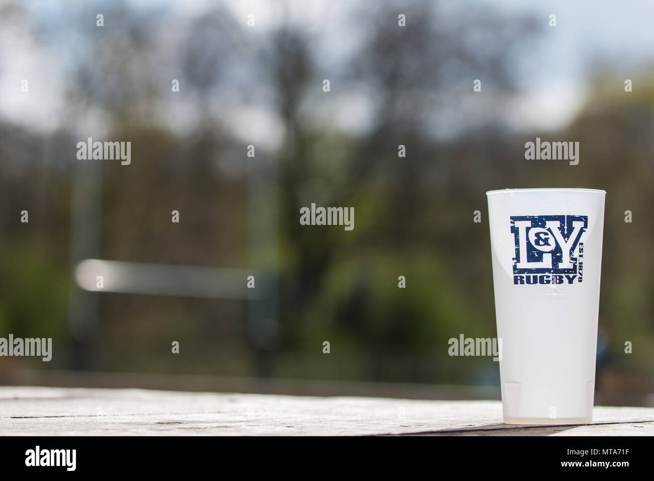Pinta di plastica vetro posto sul tavolo di legno, il logo di Lowestoft & Yarmouth Rugby Club sul vetro e il rugby posti al di fuori della messa a fuoco in background Foto Stock