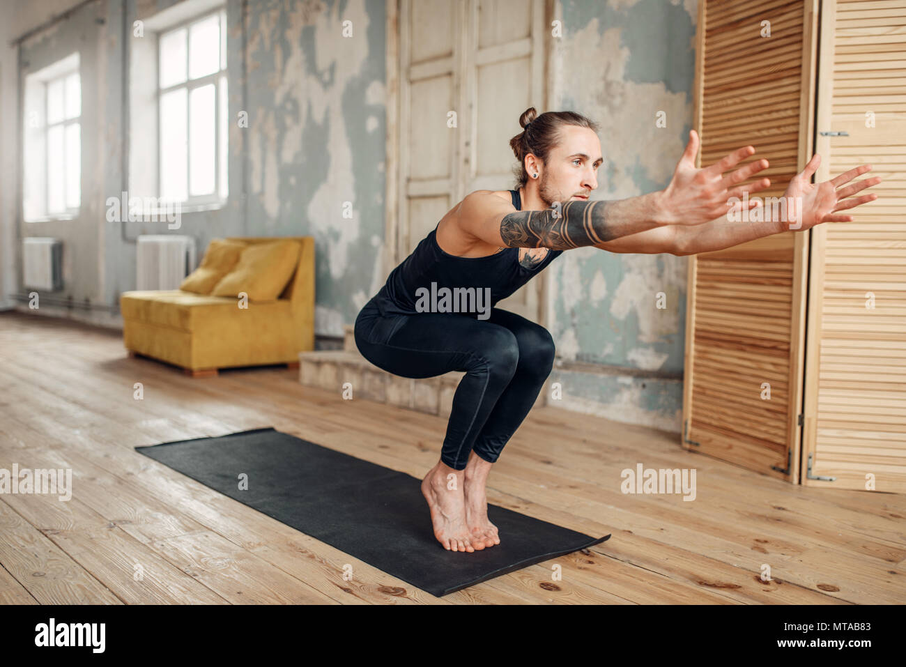 Yoga maschio con tatuaggio sul lato facendo esercizio di equilibrio sul tappeto in palestra con grunge interni. Montare l'allenamento al chiuso Foto Stock