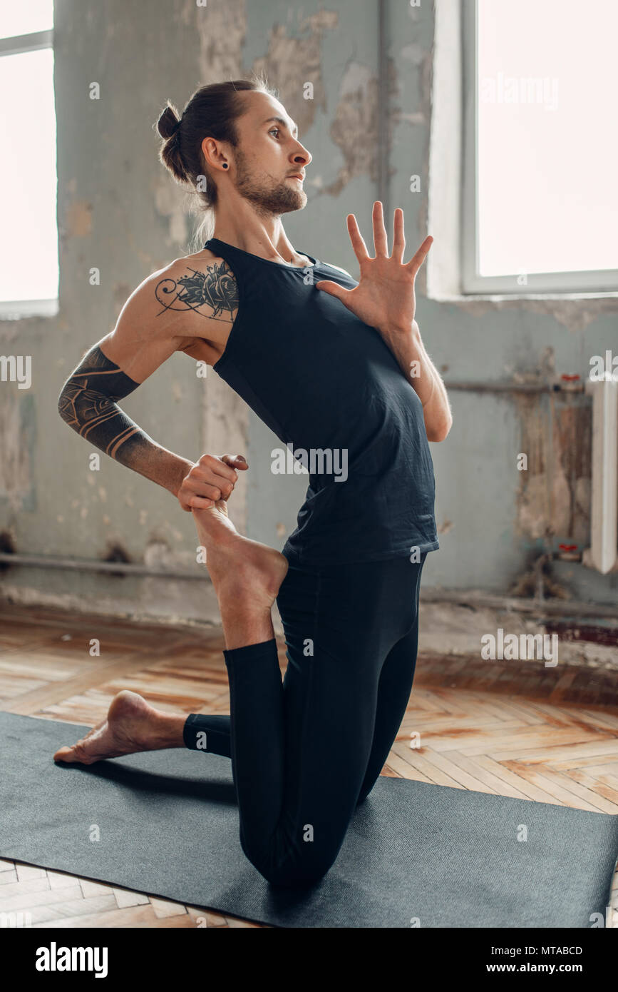 Yoga maschio in classe, la flessibilità della formazione. Esercizio sul tappeto in palestra con grunge interni. Montare l'allenamento al chiuso Foto Stock