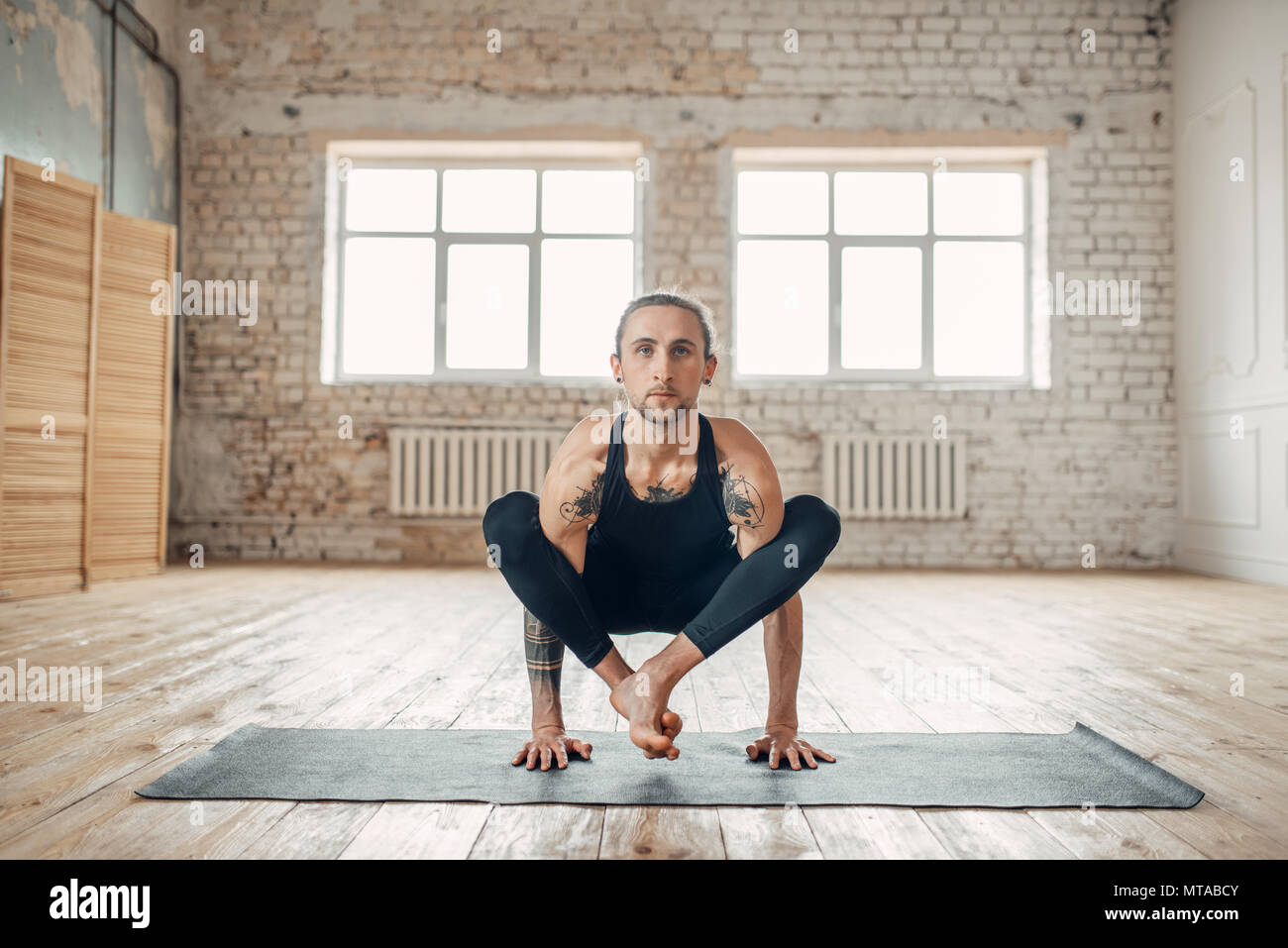Yoga maschio in classe, l'equilibrio di formazione. Esercizio sul tappeto in palestra con grunge interni. Montare l'allenamento al chiuso Foto Stock