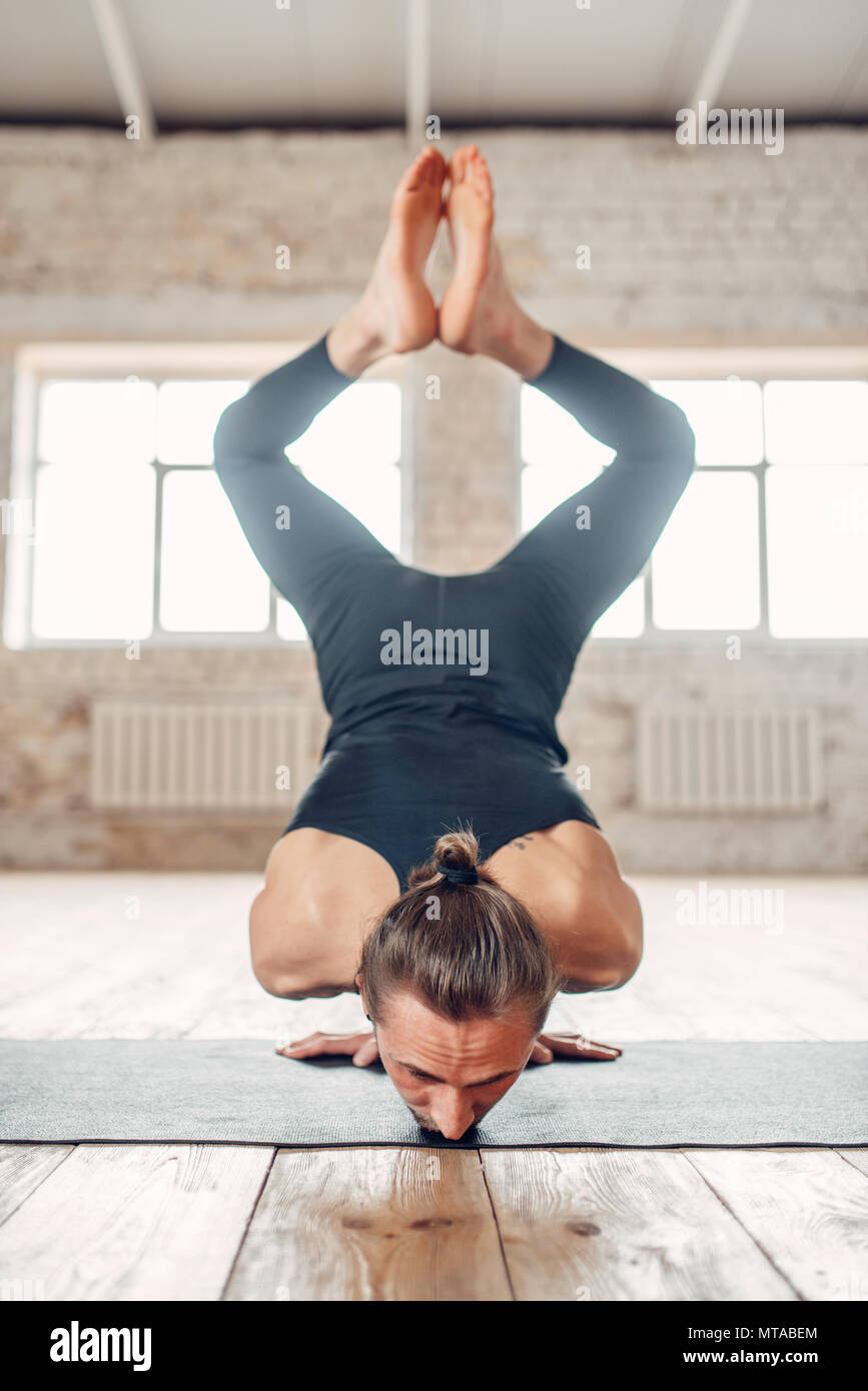 Yoga maschio in piedi sulle mani capovolto. Esercizio sul tappeto in palestra con grunge interni. Montare l'allenamento al chiuso Foto Stock