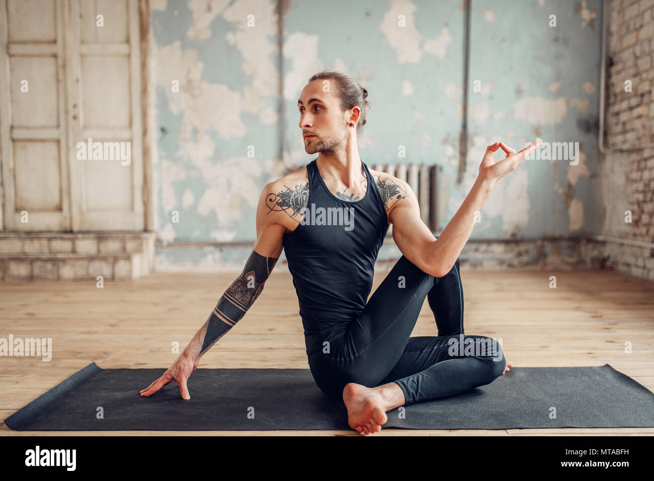 Yoga maschio facendo esercizio di flessibilità sul tappeto in palestra con grunge interni. Montare l'allenamento indoor, yogi studio Foto Stock