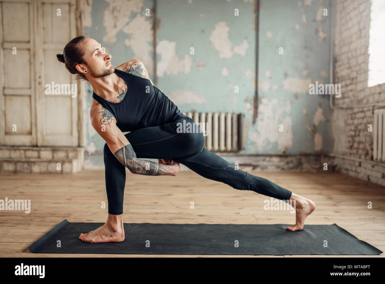 Yoga maschio facendo esercizio di flessibilità sul tappeto in palestra con grunge interni. Montare l'allenamento indoor, yogi studio Foto Stock