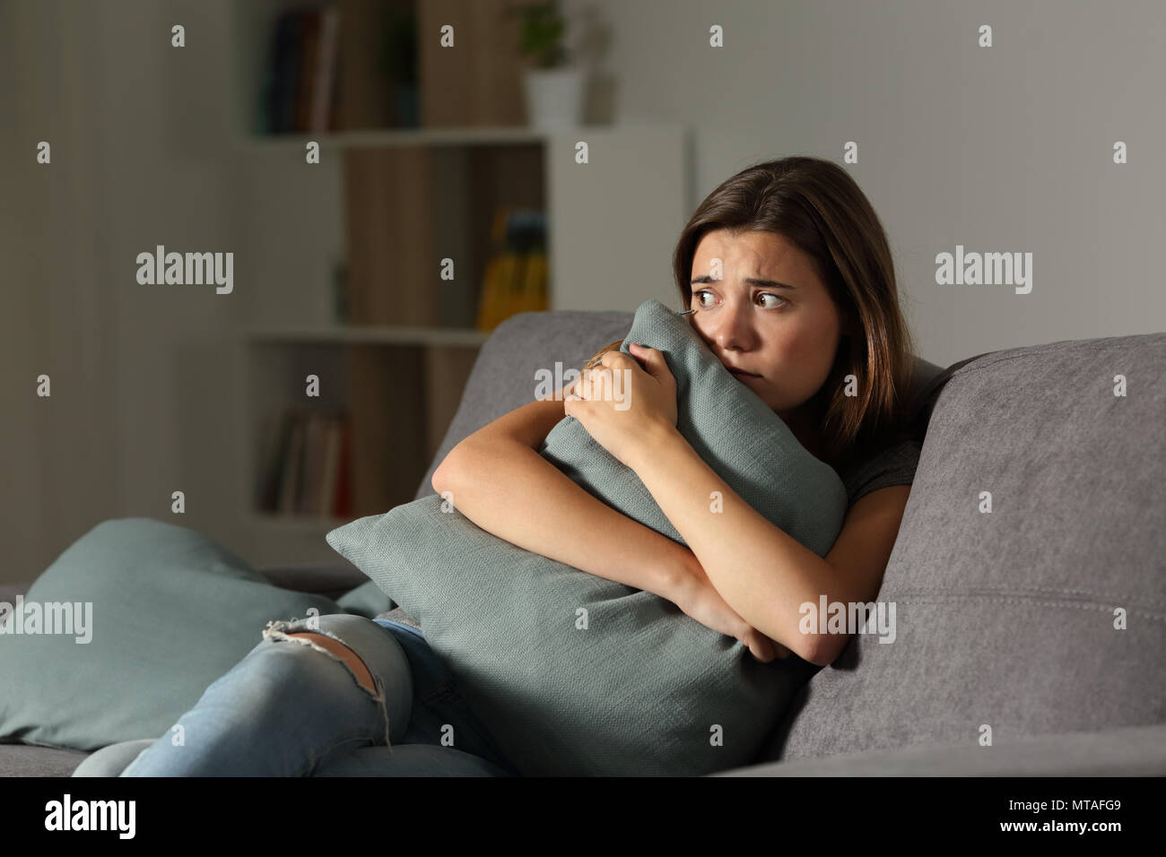 Spaventata teen in casa abbracciando cuscino seduta su un divano nel salotto di casa Foto Stock