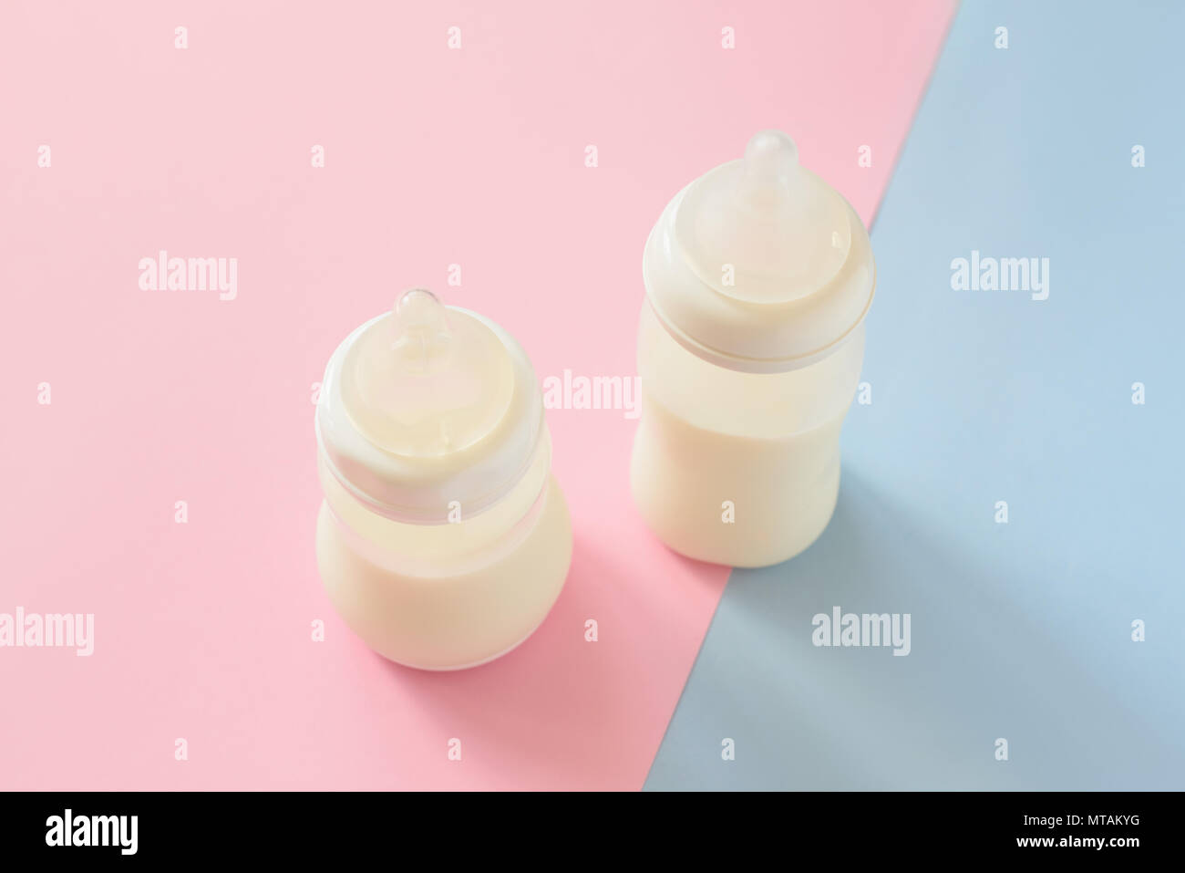 Bottiglia di latte per neonati su rosa e blu pastello sfondo. La maternità e la cura del bambino concetto. Vista dall'alto. Foto Stock